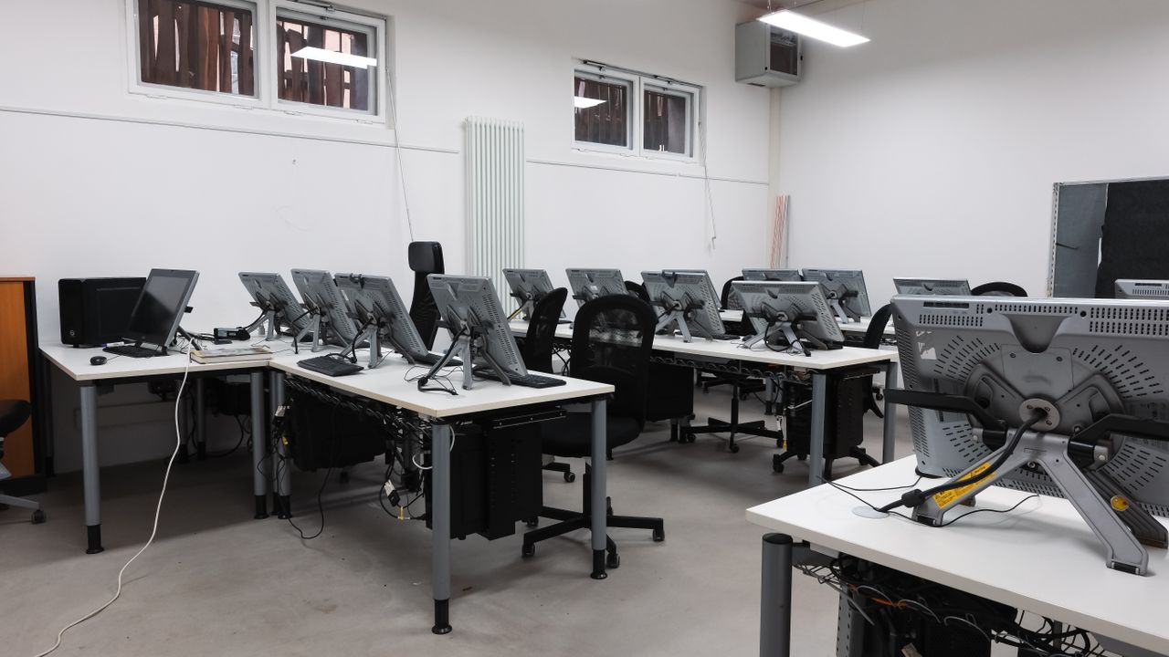About An empty computer lab featuring multiple vacant workstations with modern monitors.